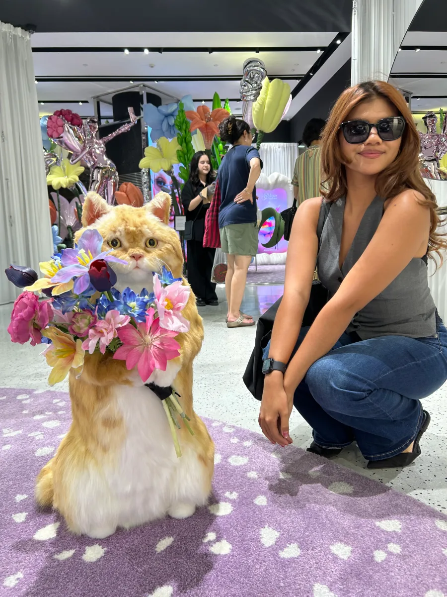 Cercie crouching beside a flower-covered cat sculpture at an exhibit
